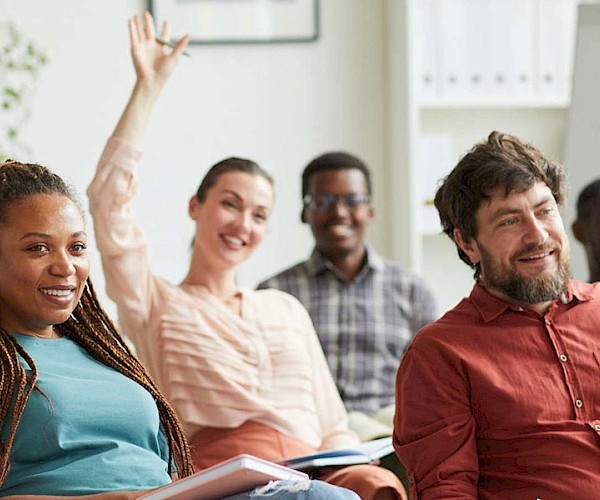 Woamn raising her hand in a meeting surrounded by other adults