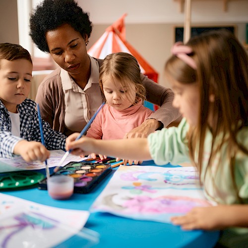 BAME woman looking on a three children painting