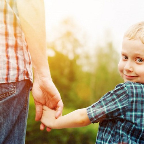 Young boy peering over his shoulder and holding a man's hand