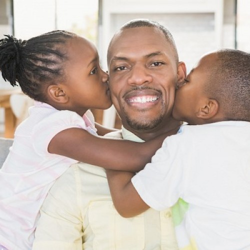 BAME man being kissed on each cheek by a young boy and girl of BAME origin