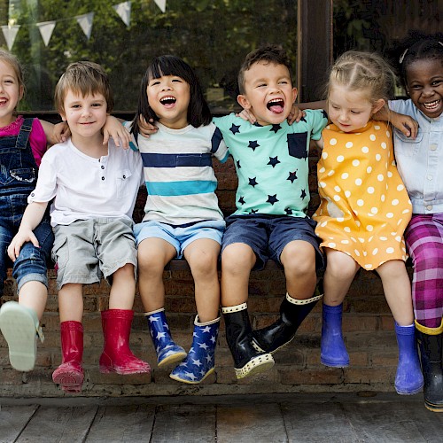 Group of young mutli ethnic children sitting on a bench and laughing together